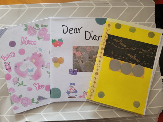 Three handmade zines published by young people, fanned out on a light coloured surface. 