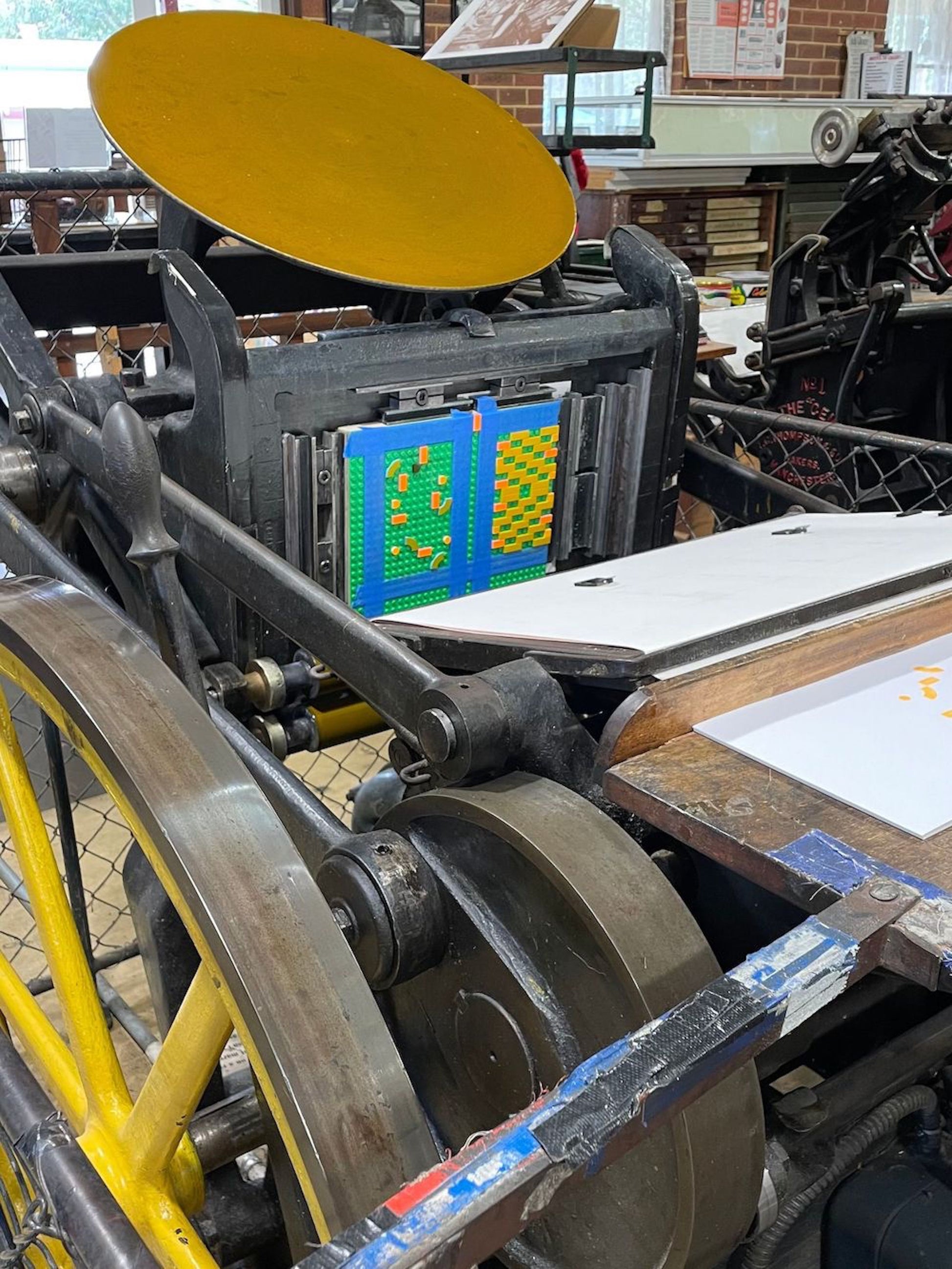 Printing press with a yellow platen and paper being printed.