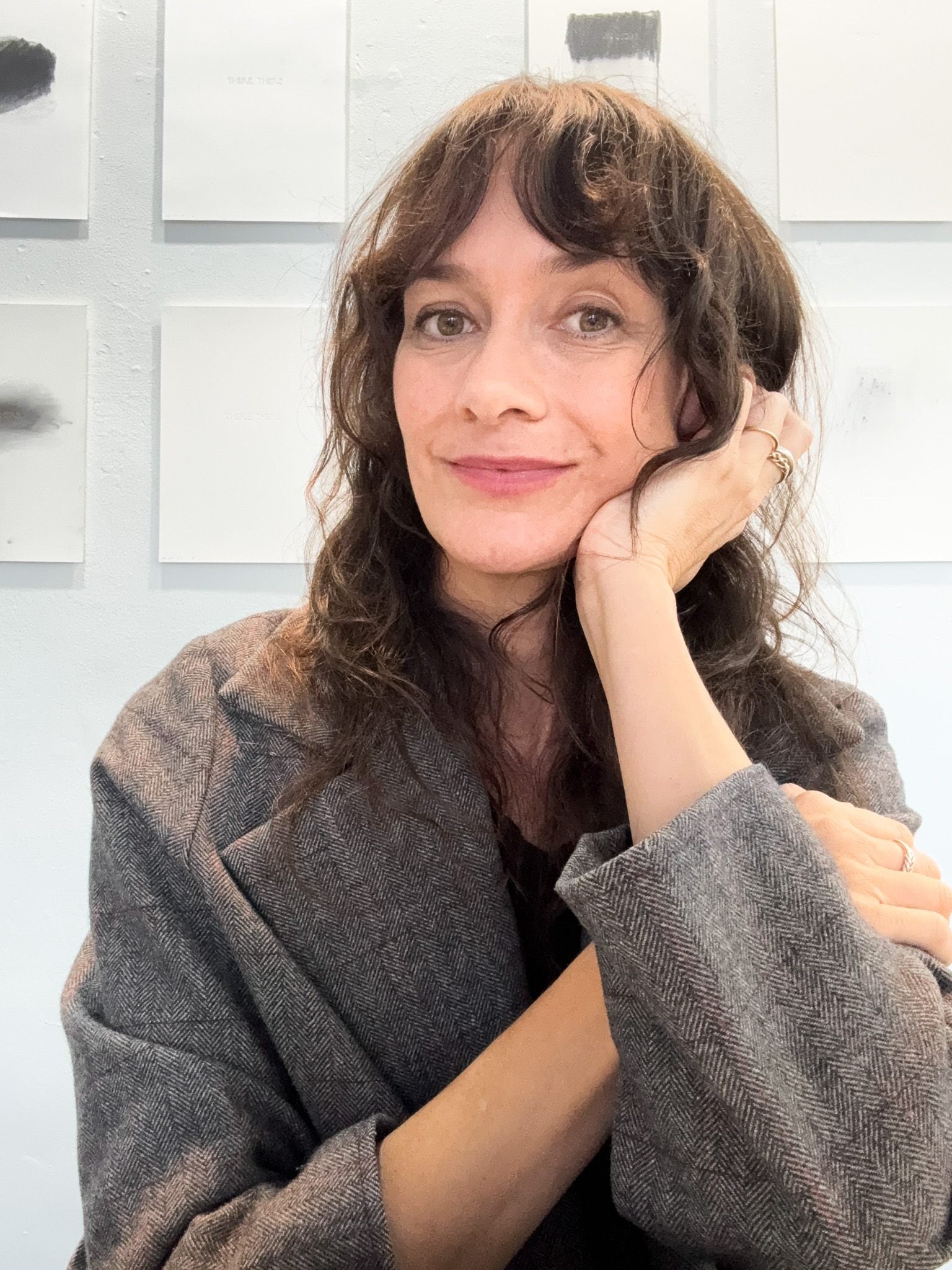 Beth George wearing a gray jacket with her artwork on a wall in background