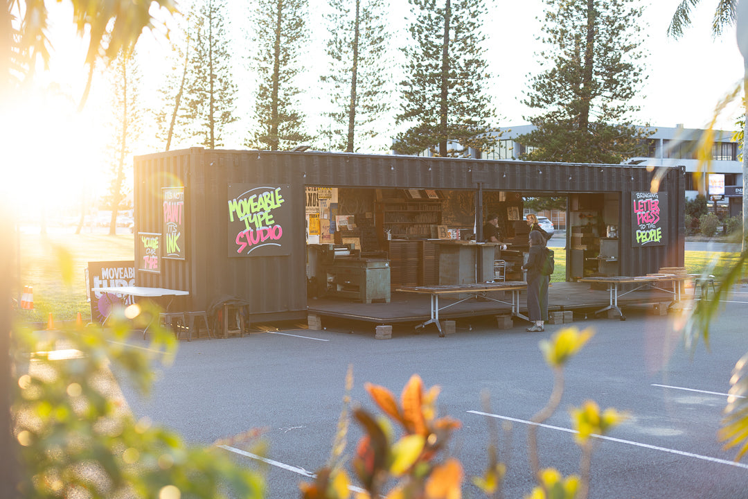 Container studio with 'Moveable Type Studio' branding in a sunlit outdoor setting.