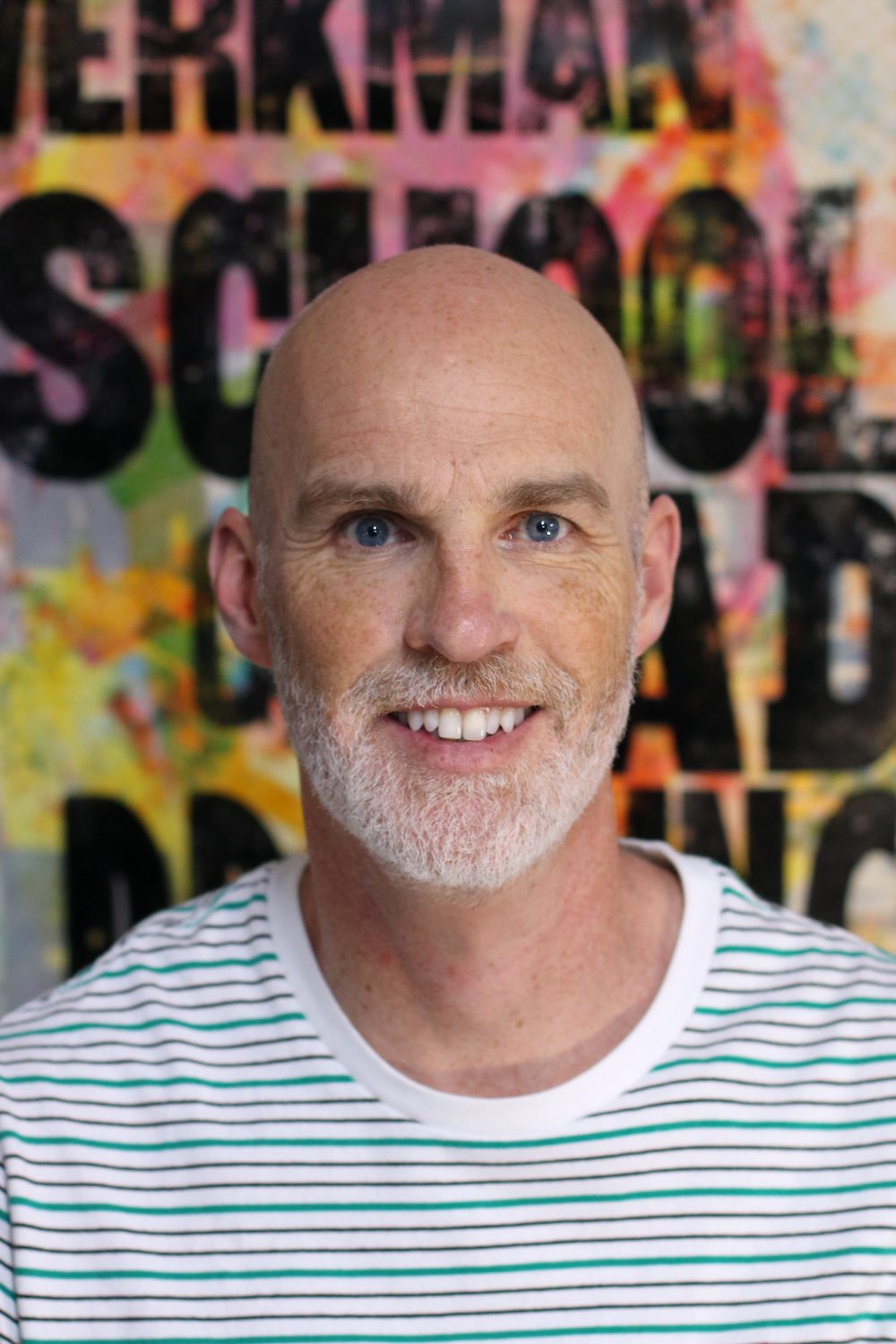 Phil Gambrill, a man with a beard wearing a striped shirt in front of a colorful background