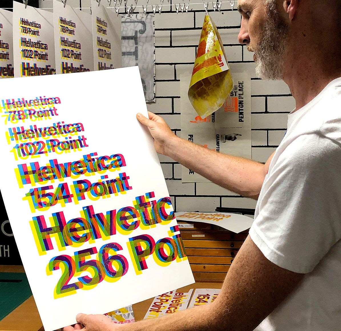 Phil holding a poster with colourful Helvetica text in his print studio
