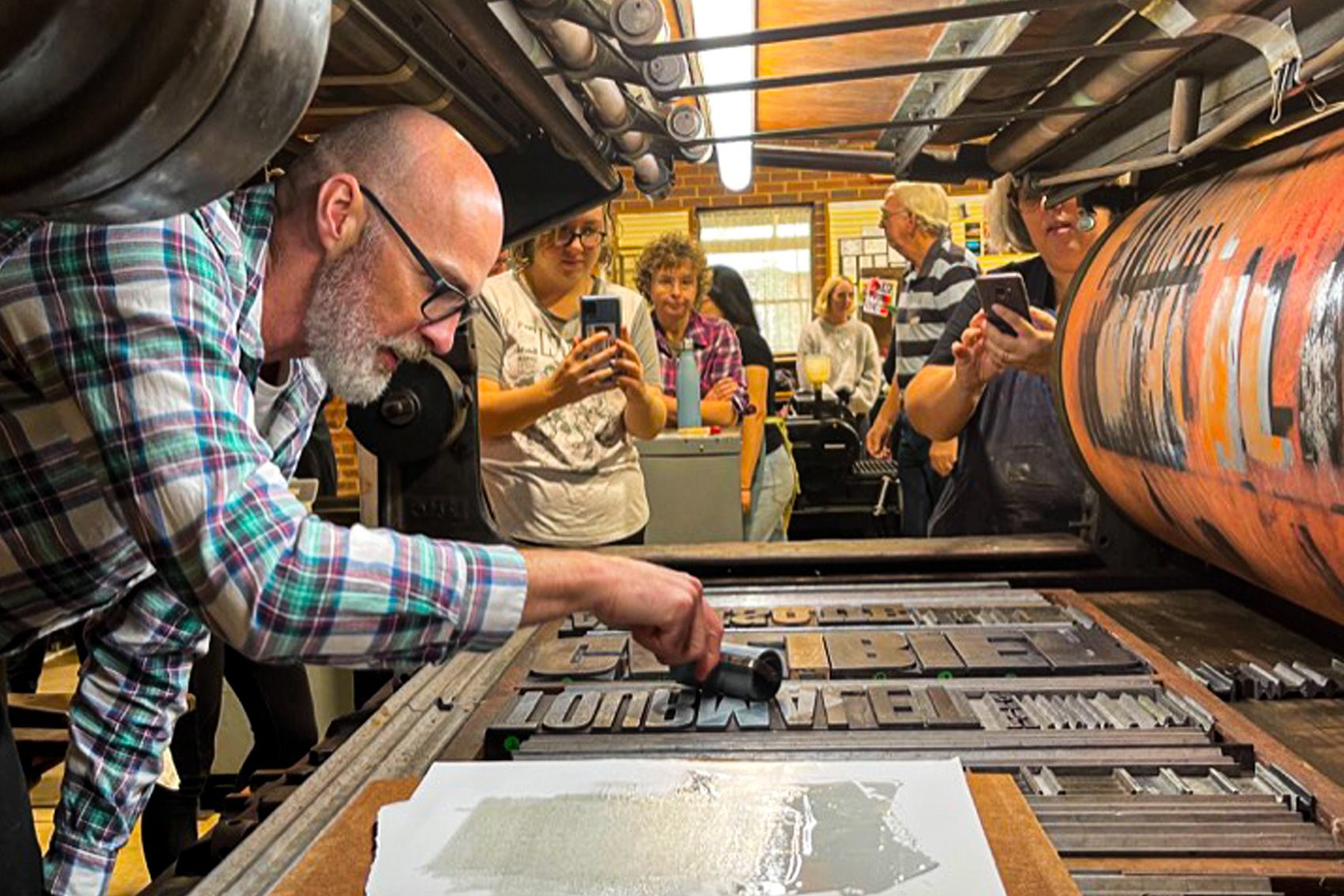 Phil Gambrill inking up in a printing forme of wood type in the belly of a quad crown Miehle press. 