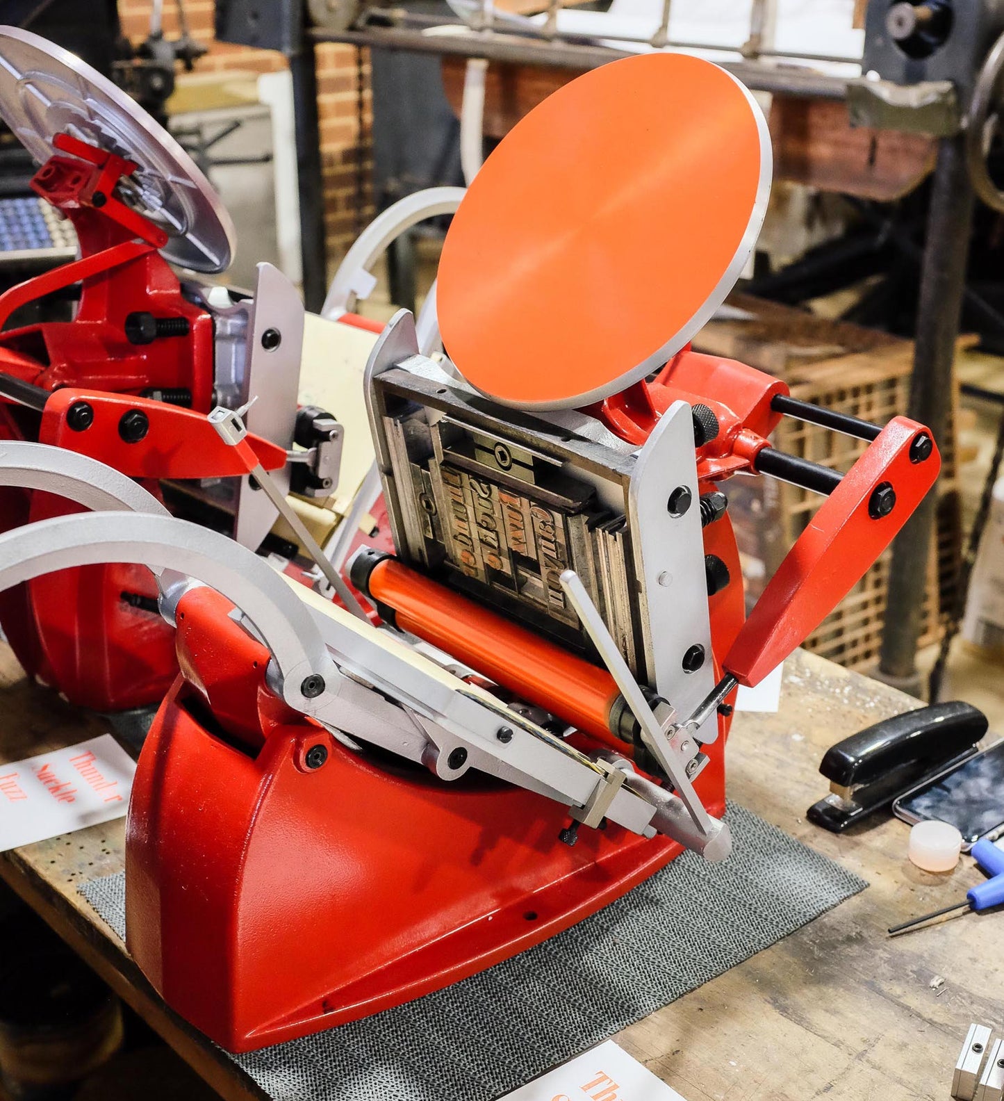 An Adana printing press with a locked up chase full of metal type and orange coloured ink on the inking disk.