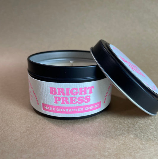 Candle in a black tin with 'Bright Press Mane Character Energy' label on a beige background
