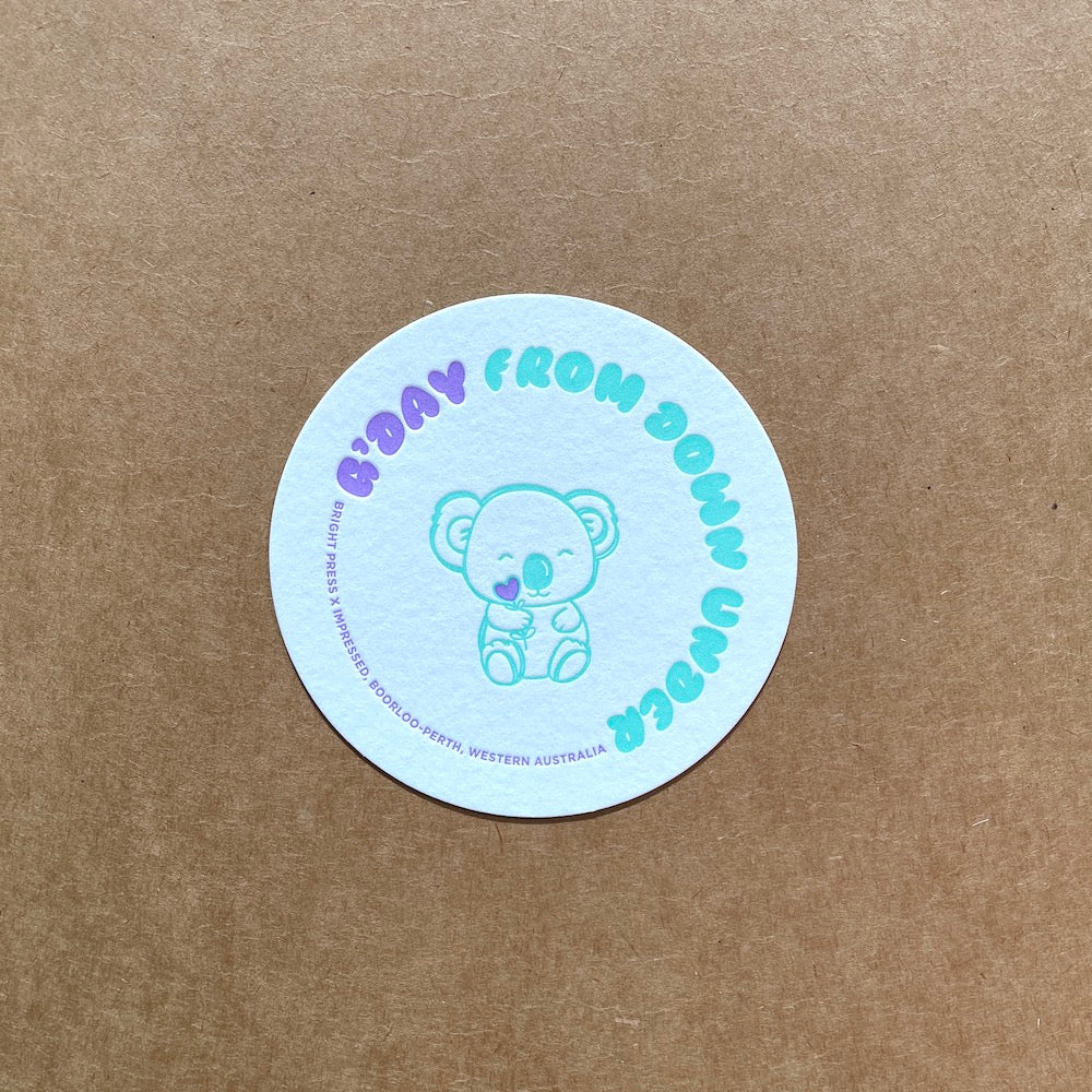 Round coaster with a koala design and text on a brown background