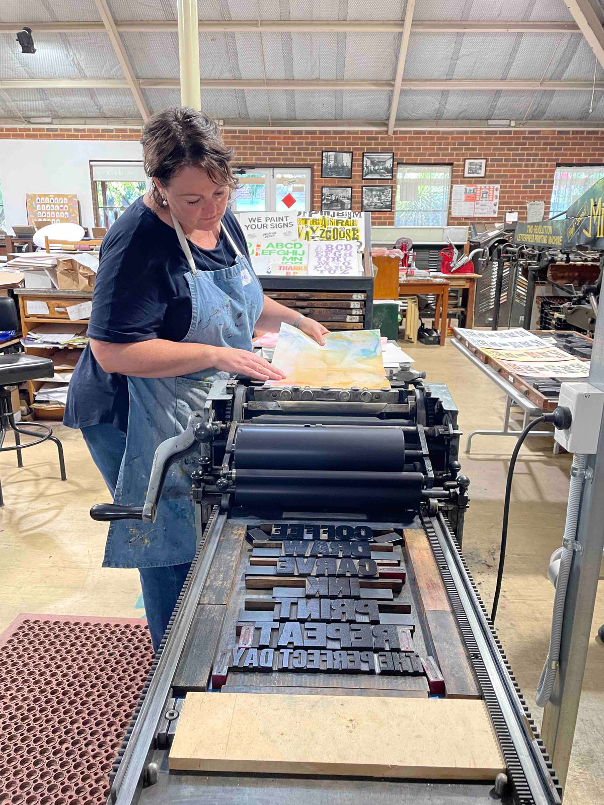 A participant feeding paper into our Vandercook press to pull a print of their poster.