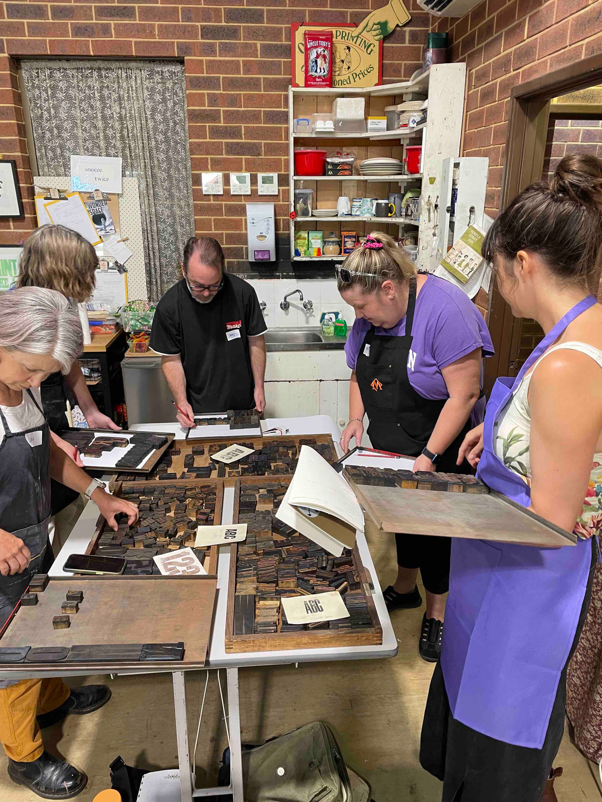 five participants around several cases of wood type selecting type for their posters.