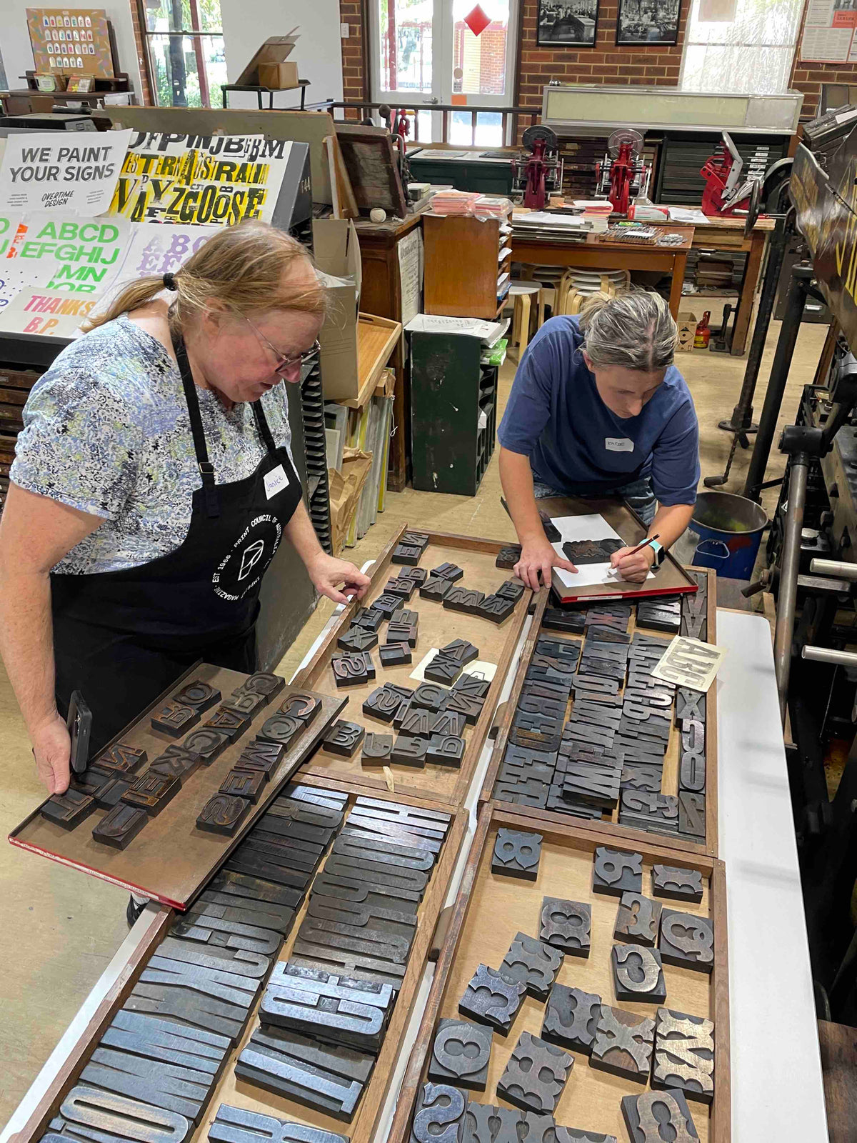 Two participants going through several cases of wood type to pick out type for their posters.