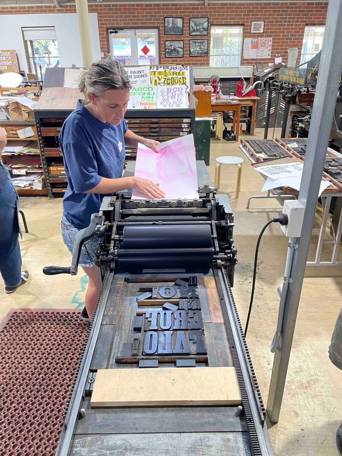 A participant feeding their pink coloured paper into the press in preparation to print.