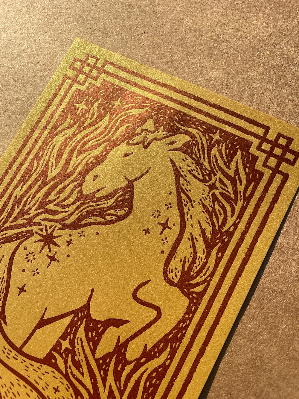 Close up of the horse illustration printed with dark red ink on metallic gold paper on a brown background