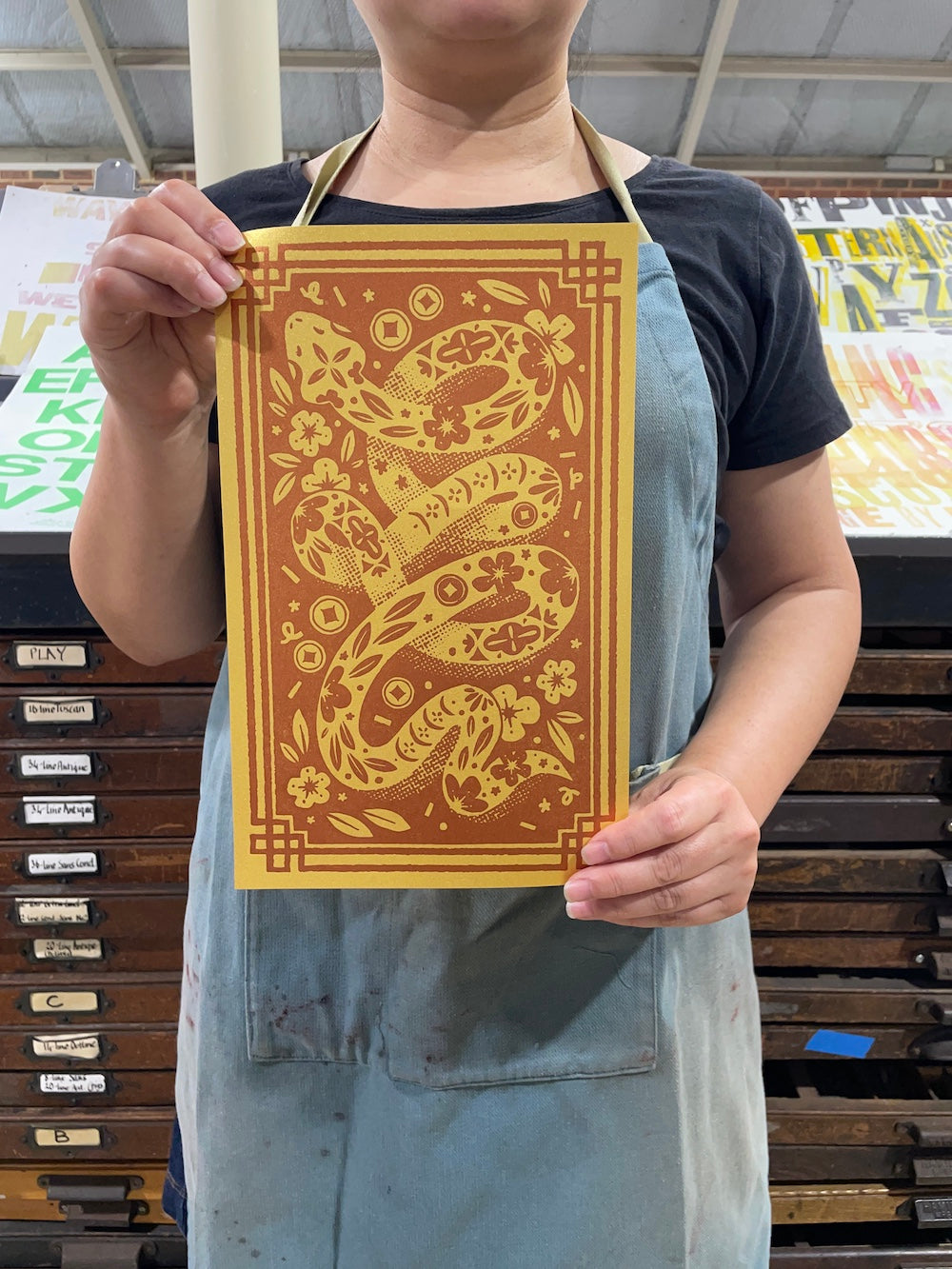 Ann is holding a print with a snake design in the print shop.