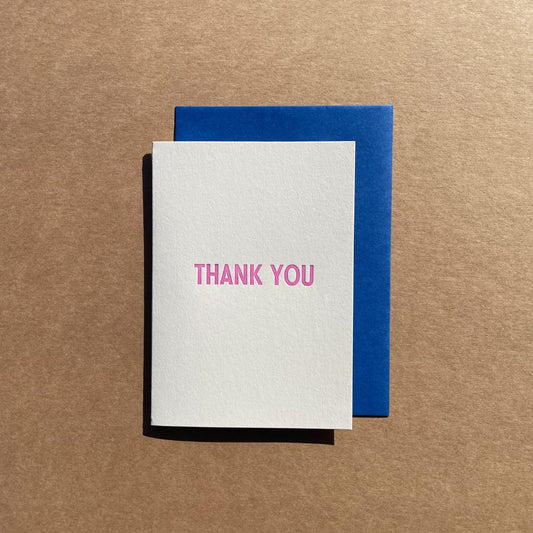 Greeting card text reading "THANK YOU" printed in purple-pink ink. Card is paired with a cobalt blue envelope.