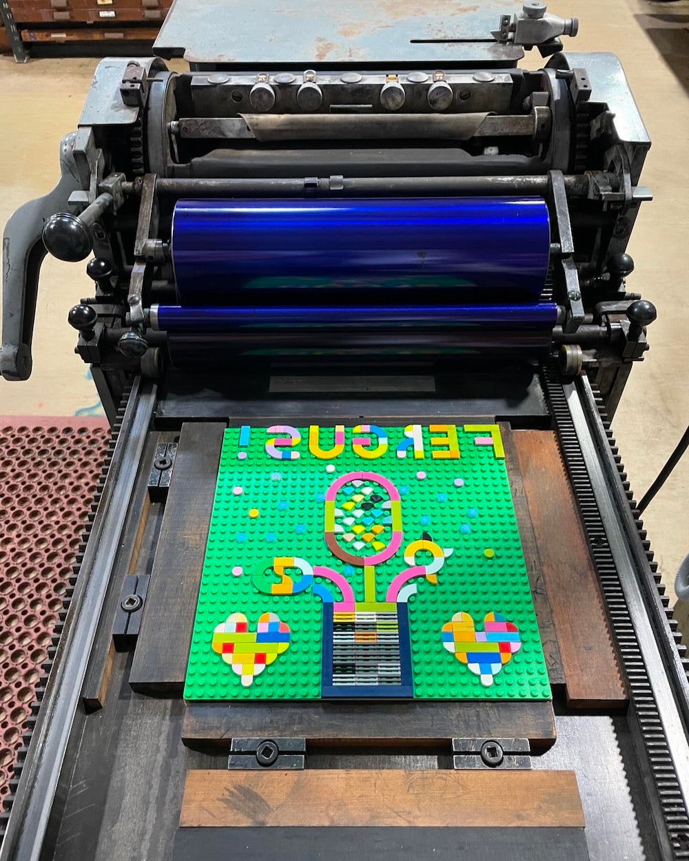 A floral arrangement with love hearts on either side of the vase, and text reading "Fergus" created with lego tiles on the printing press.