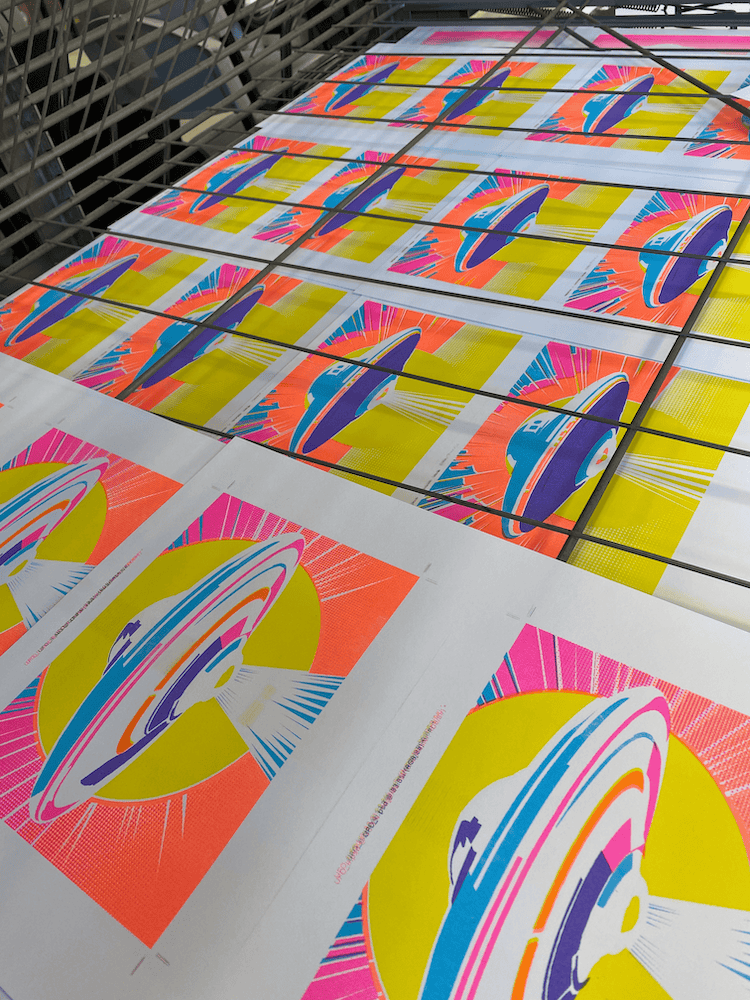 Bright fluoro coloured UFO prints by P. James Bryans on a drying rack. 